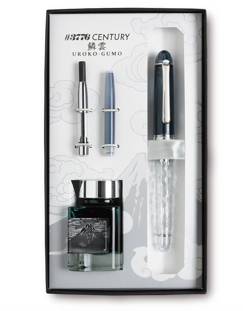 May include: A black and silver fountain pen with a clear, textured barrel. The pen is in a box with a bottle of ink and two cartridges. The box has a white background with a mountain design and the text "#3776 CENTURY 鱗雲 UROKO-GUMO".