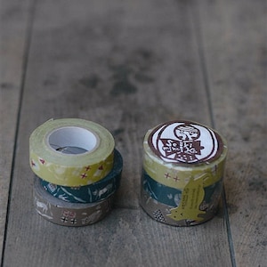 May include: A stack of three washi tapes with a yellow tape on top, a green tape in the middle, and a brown tape on the bottom. The top tape has a brown stamp with the text "Seki Miho Ko" in white. The tapes are on a wooden surface.