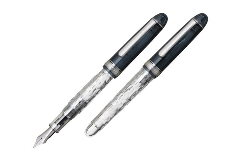 May include: Two silver and blue fountain pens with a textured design. The pens have a clear barrel and a silver cap.