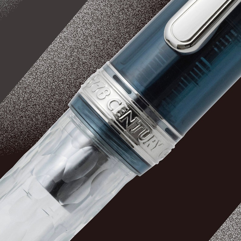 May include: Close-up of a blue and silver fountain pen with the inscription "148 Century" on the cap.