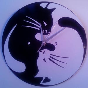 May include: A black and white yin yang clock with a silver clock hand. The yin yang symbol is made up of two cats facing each other. The clock face has the numbers 3, 6, 9, and 12.