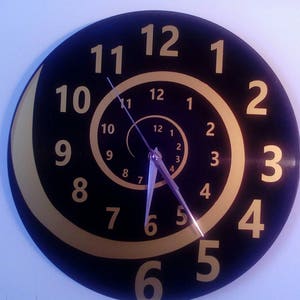 Könnte beinhalten: Eine schwarze Schallplattenuhr mit goldenen Zahlen in einem Spiralmuster. Die Uhrzeiger sind silberfarben.