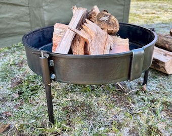 May include: A black metal fire pit with three legs, sitting on a grassy surface covered in frost. The fire pit is filled with pieces of firewood.