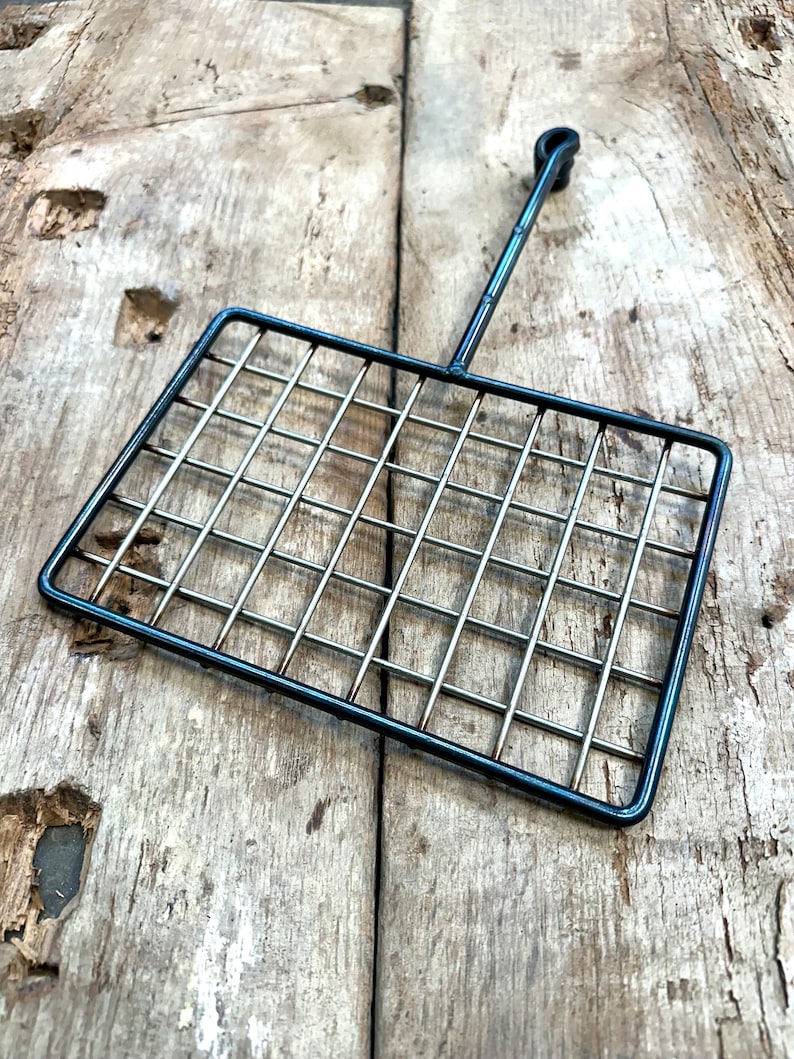 May include: A black metal grilling basket with a rectangular grid design and a long handle. The basket is made of thin metal rods and is designed for grilling food. The handle has a loop at the end for hanging.