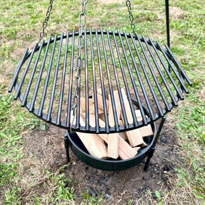 Puede incluir: Un hogar de fuego colgante de metal negro con una rejilla redonda y una base llena de leña.