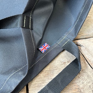 Pode incluir: Uma bolsa tote preta com uma bandeira do Reino Unido bordada na frente. A bolsa tem duas al&ccedil;as pretas e &eacute; feita de um tecido resistente.