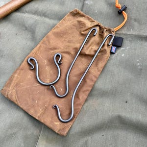 May include: Three metal hooks with a decorative curl at the end, in a brown canvas bag with a black label and an orange drawstring.