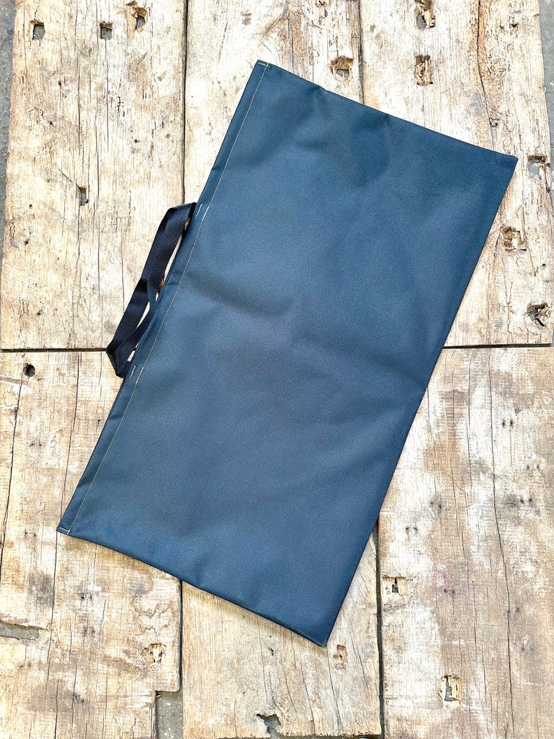 Pode incluir: Uma bolsa tote de lona azul escura com al&ccedil;as pretas. A bolsa est&aacute; deitada sobre uma superf&iacute;cie de madeira.
