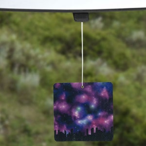 May include: A car air freshener with a galaxy design. The design features a dark blue background with pink, purple, and blue nebulae.