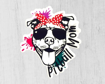 May include: A white pitbull dog wearing sunglasses and a red and white polka dot bandana with the word "Mom" written on the side. The dog is sticking its tongue out and has green and pink paint splatters around it. The words "Pitbull Mom" are written in a green and white font.