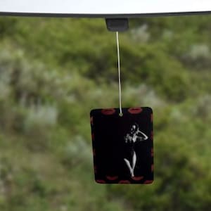 May include: A black and white car air freshener with a red lip design. The air freshener features a silhouette of a person dancing.