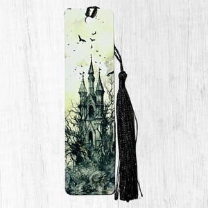 May include: A gothic bookmark with a detailed illustration of a haunted castle with tall spires, surrounded by bare trees and flying bats. A black tassel hangs from the top. The color palette is primarily black, grey, and cream.