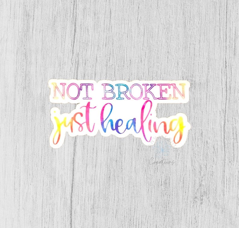 以下が含まれることがあります： 虹色のグラデーションで「NOT BROKEN just healing」というテキストが書かれたカラフルなステッカー。ステッカーは白い背景の上にあります。