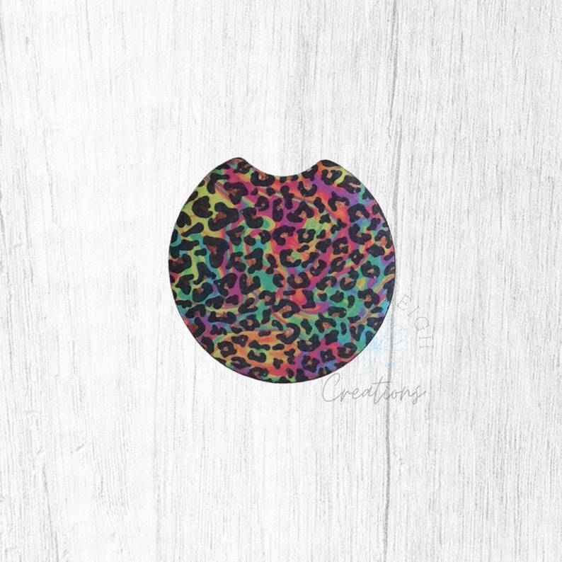 May include: Round car coaster with a colorful leopard print design. The print features a rainbow of colors including pink, orange, yellow, green, blue, and purple. The background is black.