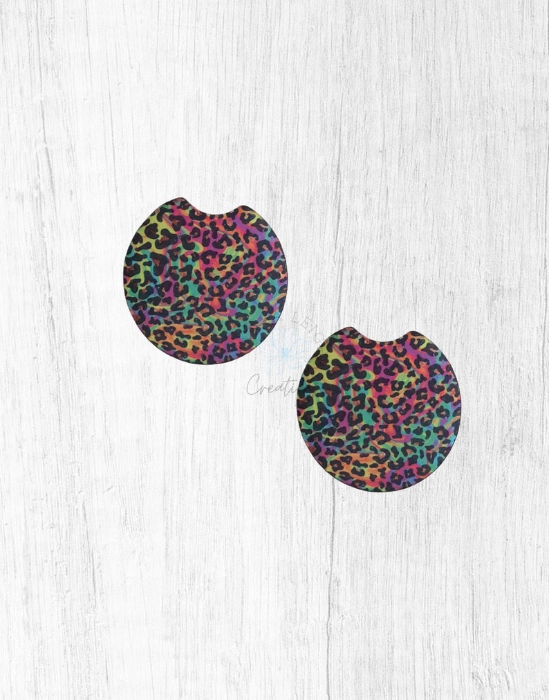 May include: Two round, black coasters with a rainbow leopard print design.