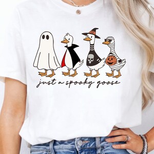 a woman wearing a white t - shirt that says just a spooky goose