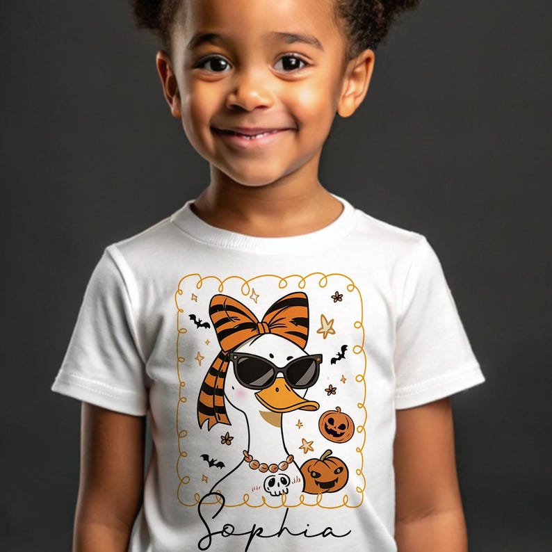 Op de afbeelding: Wit T-shirt met een cartoon gans met een zonnebril, een strik en een ketting. De gans is omringd door Halloween-thema graphics, waaronder pompoenen en vleermuizen. De naam "Sophia" staat eronder in cursief.