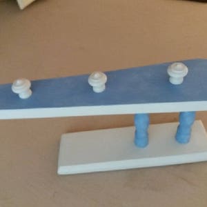 Peut inclure: Un porte-manteau en bois bleu et blanc avec trois crochets. Le porte-manteau est peint en bleu clair avec des accents blancs. Les crochets sont blancs et ronds.