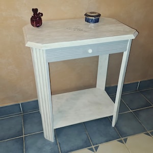 Peut inclure: Une table d'appoint blanche peinte avec un tiroir et une étagère inférieure. La table a un aspect vieilli et est décorée d'un motif floral.