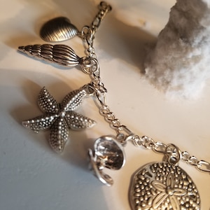 May include: A silver charm bracelet with a variety of sea-themed charms, including a seashell, a starfish, a sand dollar, and a heart.