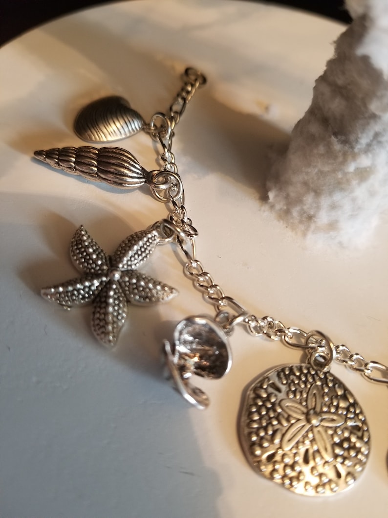 May include: A silver charm bracelet with a variety of sea-themed charms, including a seashell, a starfish, a sand dollar, and a heart.
