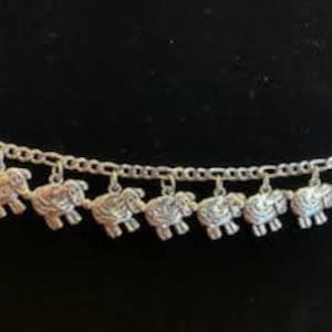 Puede incluir: Un brazalete de plata con una cadena y varios colgantes con forma de oveja.