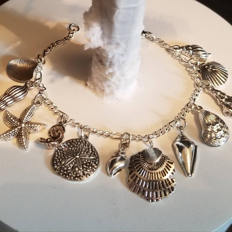 May include: A silver charm bracelet with various sea-themed charms, including a starfish, seashells, and a sand dollar.