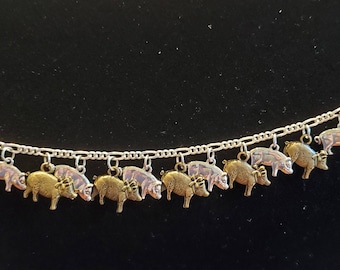May include: A silver charm bracelet with 10 pig charms. The charms are a mix of gold and silver and are all facing the same direction. The bracelet is on a black background.