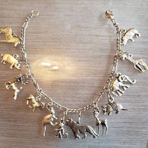 May include: A silver charm bracelet featuring a range of animal charms, including a zebra, pig, deer, elephant, giraffe, armadillo, and a tiger. The bracelet is made from a silver chain with a lobster clasp.