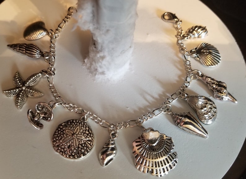 May include: Silver charm bracelet with various sea-themed charms, including seashells, starfish, and a sand dollar.