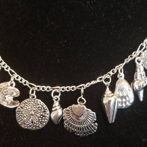 May include: A silver charm bracelet with multiple charms shaped like seashells, sand dollars, and other beach-themed designs.