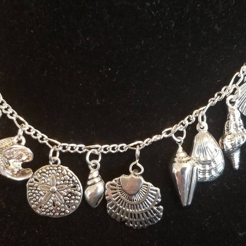 May include: A silver charm bracelet with multiple charms shaped like seashells, sand dollars, and other beach-themed designs.
