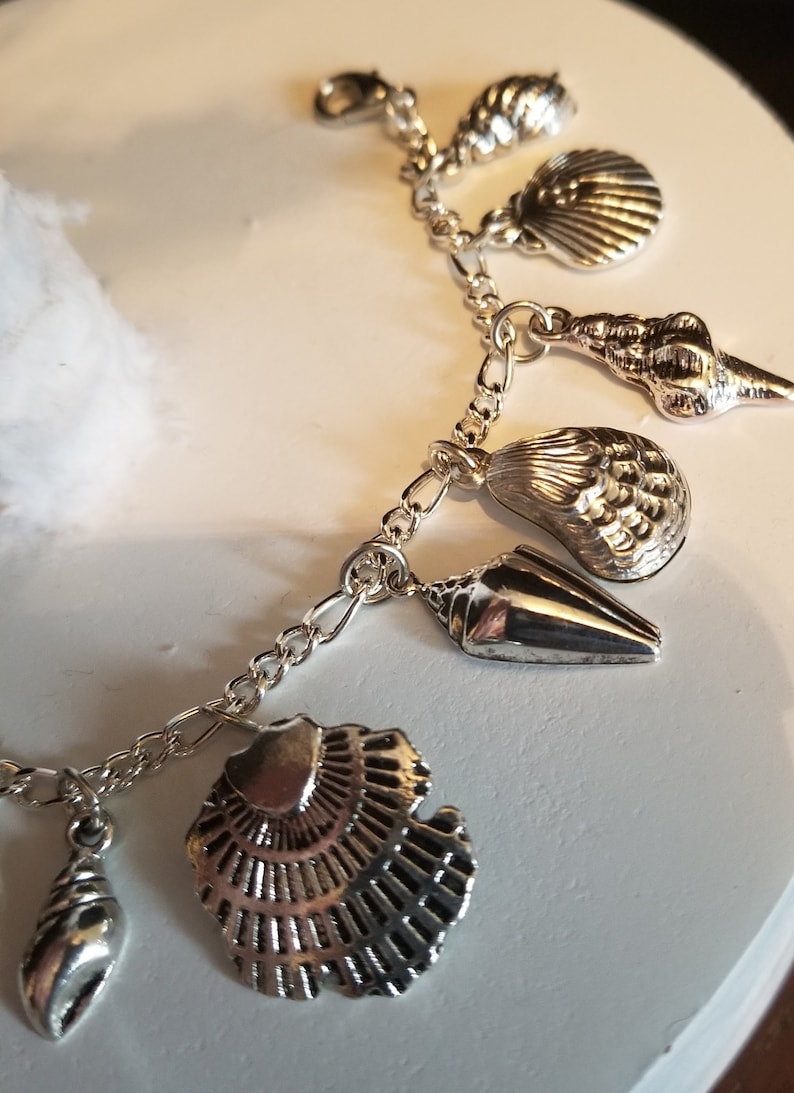 May include: A silver charm bracelet with multiple silver seashell charms. The charms are detailed and realistic.