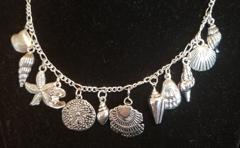 May include: A silver chain necklace with multiple charms in the shape of seashells, starfish, and sand dollars.