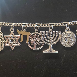 May include: A silver charm bracelet with multiple charms, including a Star of David, a menorah, a hamsa hand, and a tree of life. The charms are attached to a silver chain.