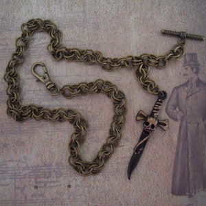 Pode incluir: Uma corrente de lat&atilde;o com um pingente de espada com caveira e ossos cruzados. A corrente tem um fecho de lagosta e um fecho girat&oacute;rio. O pingente tem aproximadamente 7,5 cm de comprimento.