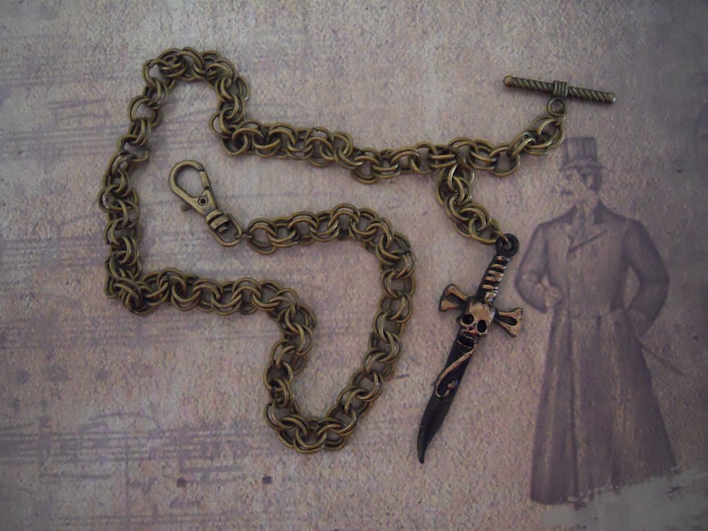 Pode incluir: Uma corrente de lat&atilde;o com um pingente de espada com caveira e ossos cruzados. A corrente tem um fecho de lagosta e um fecho girat&oacute;rio. O pingente tem aproximadamente 7,5 cm de comprimento.