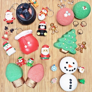 May include: A collection of Christmas-themed items, including keychains with Santa, reindeer, and snowman figures. Also shown are bath bombs, rings, and decorative ornaments in festive shapes like a Christmas tree, gingerbread man, and light bulbs.