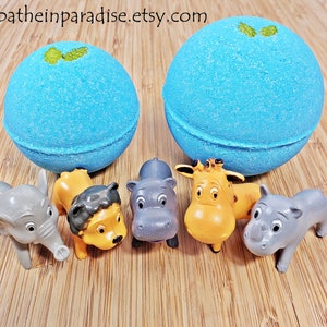 May include: Two large, round, blue bath bombs with a green accent sit above six small plastic animal toys. The toys include an elephant, lion, hippo, giraffe, and rhino. The Etsy shop name is visible at the top.