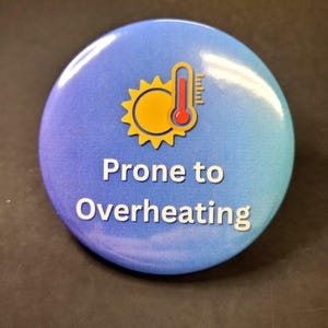 May include: A round button with a gradient blue background. The button features a yellow sun graphic with a red thermometer, and the words "Prone to Overheating" in white text.