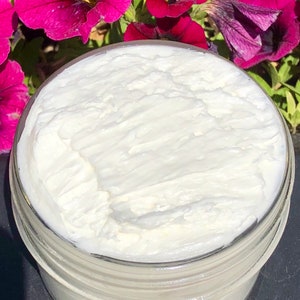 A photo of creamy body butter with its texture shown. there are pink flowers in the background