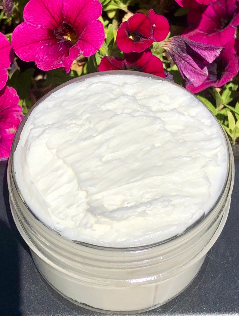 A photo of creamy body butter with its texture shown. there are pink flowers in the background