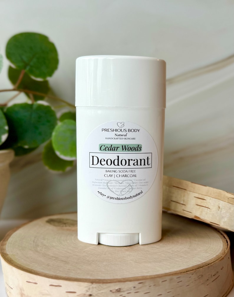 White deodorant stick with a label that reads 'PRESHIOUS BODY Natural HANDCRAFTED SKINCARE Cedar Woods Deodorant BAKING SODA FREE CLAY | CHARCOAL *etsy @preshiousbodynatural'