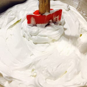 A photo of creamy body butter with its texture shown. there is a spoon standing upright in the body butter to show its thickness and consistency