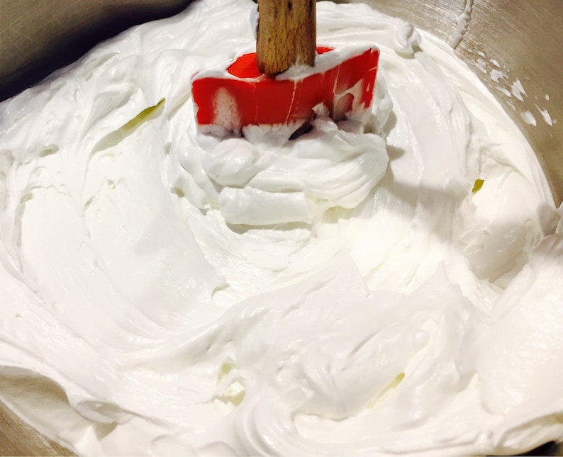 A photo of creamy body butter with its texture shown. there is a spoon standing upright in the body butter to show its thickness and consistency