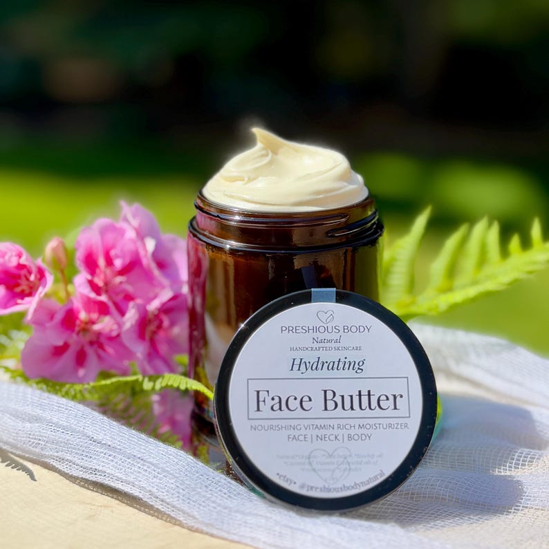 May include: A glass jar with a black lid filled with a face butter. The jar has a white label with the text 'PRESHIOUS BODY', 'Natural', 'HANDCRAFTED SKINCARE', 'Hydrating', 'Face Butter', 'NOURISHING VITAMIN RICH MOISTURIZER', 'FACE | NECK | BODY', 'Natural Organic Shea butter Rosehip oil Coconut Vitamin E Essential oils of Frankincense Lavender', 'etsy. @preshiousbodynatural'.