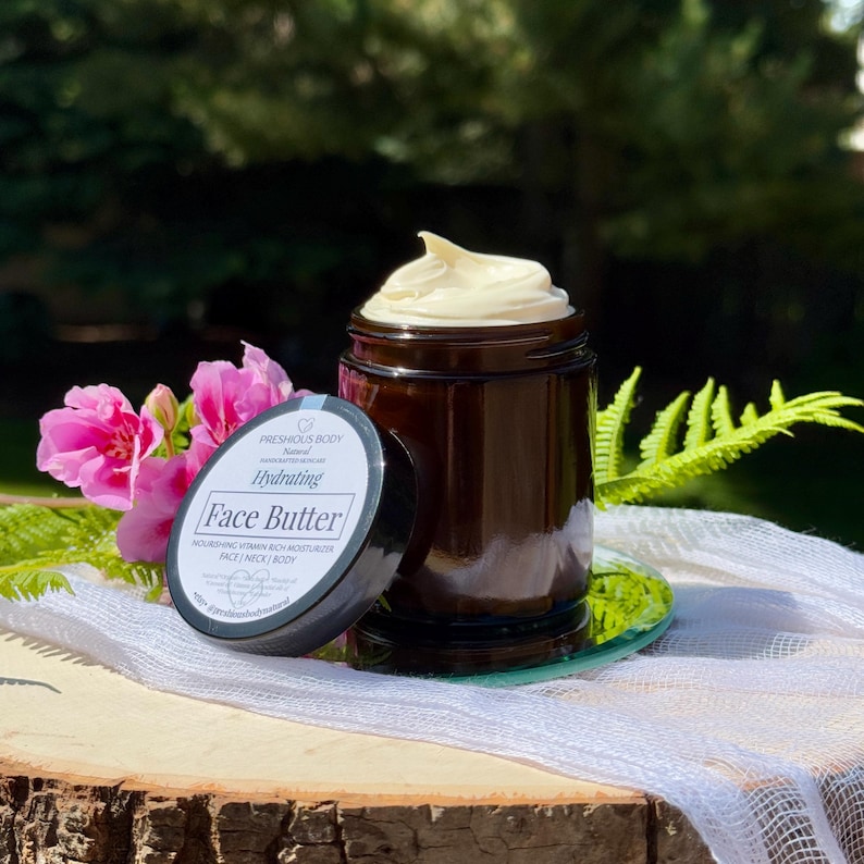 May include: A glass jar with a black lid filled with a face butter. The jar has a white label with the text 'PRESHIOUS BODY', 'Natural', 'HANDCRAFTED SKINCARE', 'Hydrating', 'Face Butter', 'NOURISHING VITAMIN RICH MOISTURIZER', 'FACE | NECK | BODY', 'Natural Organic Shea butter Rosehip oil Coconut Vitamin E Essential oils of Frankincense Lavender', 'etsy. @preshiousbodynatural'.