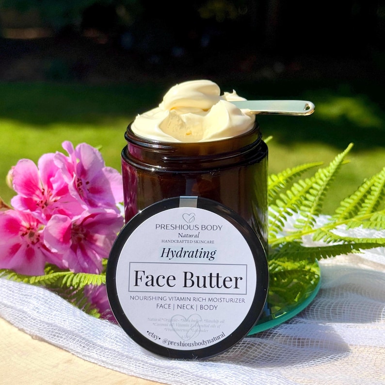 May include: A glass jar with a black lid filled with a face butter. The jar has a white label with the text 'PRESHIOUS BODY', 'Natural', 'HANDCRAFTED SKINCARE', 'Hydrating', 'Face Butter', 'NOURISHING VITAMIN RICH MOISTURIZER', 'FACE | NECK | BODY', 'Natural Organic Shea butter Rosehip oil Coconut Vitamin E Essential oils of Frankincense Lavender', 'etsy. @preshiousbodynatural'.