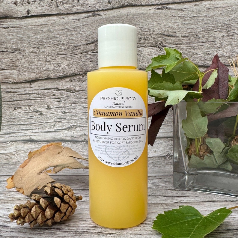 A bottle of body serum with a white label. The label says 'Preshious Body Natural Handcrafted Skincare Cinnamon Vanilla Body Serum Nourishing Antioxidant Rich Moisturizer for Soft Smooth Skin *ctay @preshiousbodynatural'