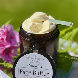 May include: A glass jar with a black lid filled with a face butter. The jar has a white label with the text 'PRESHIOUS BODY', 'Natural', 'HANDCRAFTED SKINCARE', 'Hydrating', 'Face Butter', 'NOURISHING VITAMIN RICH MOISTURIZER', 'FACE | NECK | BODY', 'Natural Organic Shea butter Rosehip oil Coconut Vitamin E Essential oils of Frankincense Lavender', 'etsy. @preshiousbodynatural'.